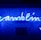 A bright blue neon sign spells out the word 'gambling' in cursive script. The background features a textured wall covered in domino tiles, also illuminated by the blue light, creating a vivid and visually striking scene.