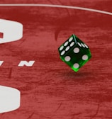 Two green dice with rounded edges are positioned on a red surface that seems to be part of a game board. The surface has white text and numbers on it, including the word 'LUCKYTOPSPIN' in capital letters.