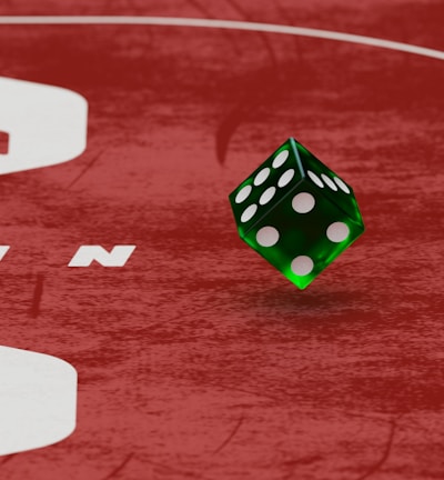 Two green dice with rounded edges are positioned on a red surface that seems to be part of a game board. The surface has white text and numbers on it, including the word 'LUCKYTOPSPIN' in capital letters.