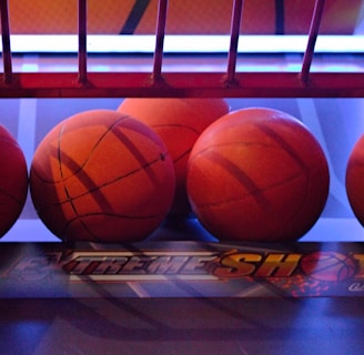 Several basketballs are aligned in a row on a basketball arcade machine platform. The environment has a colorful and illuminated backdrop with a mix of red and blue lighting.
